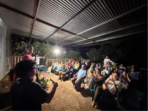 An evening gathering with people seated together under an open-sided roof