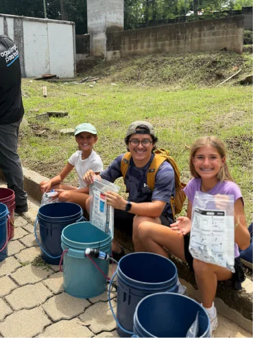 Three volunteers preparing buckets and supplies outdoors