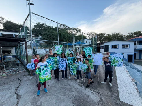 Children and volunteers displaying colorful painted shirts outdoors